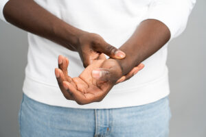 Man in white sweatshirt and jeans holding his painful wrist